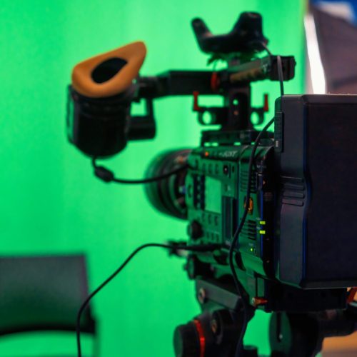 Professional video camera on a stand with green chromakey in a studio